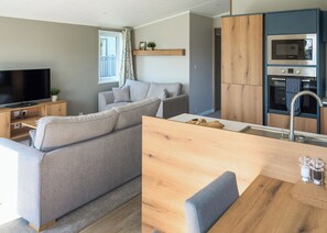 A modern living space with a sofa, TV, wooden cabinets, and a kitchen area.