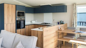 Moderni keittiö, jossa on puukalusteet, sisäänrakennettu uuni sekä ruokailutila pöytineen ja tuoleineen.