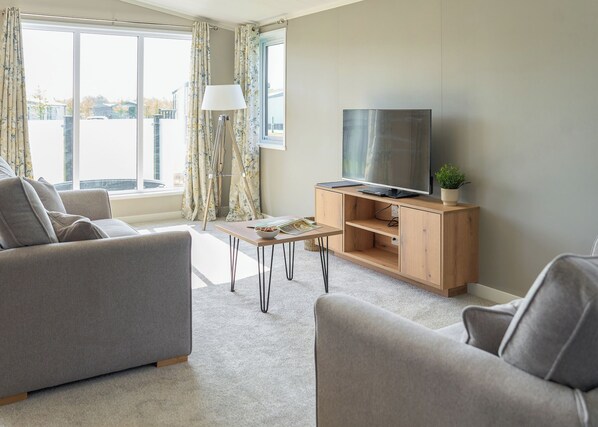 A modern living room with a sofa, a coffee table, a TV on a wooden stand, and a window with curtains.