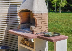 A brick-built outdoor oven with a chimney, a grill, and a metal tray on a concrete stand. - 1 bedroom accommodation in Landford, Nr Salisbury (Landford, Nr Salisbury)