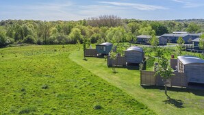 A campsite with several wooden cabins, a grassy field, and a forested area in the background. - 1 bedroom accommodation in Landford, Nr Salisbury (Landford, Nr Salisbury)