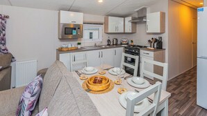 A compact kitchen with a microwave, stove, and sink, a dining table set with plates and cutlery, and a sofa with patterned cushions.