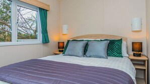 A bedroom with a bed, two bedside tables with lamps, a window with curtains, and a wall-mounted light fixture.