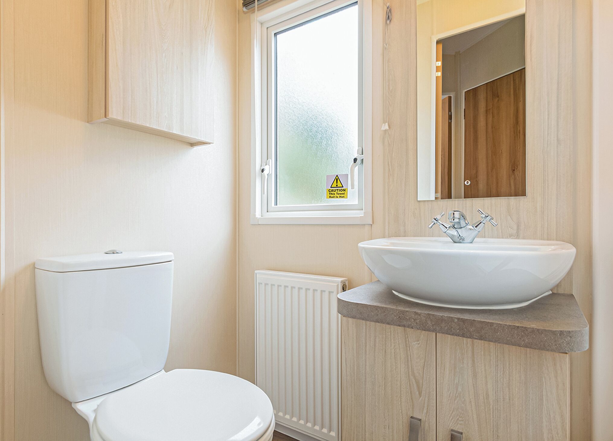 Une salle de bain moderne comprenant des toilettes, un lavabo blanc avec un receveur, une fenêtre à verre dépoli et un miroir au-dessus du lavabo.