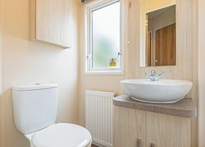 A modern bathroom with a toilet, a white sink with a vessel basin, a window with frosted glass, and a mirror above the sink.