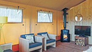 Une pièce chaleureuse aux murs en bois, dotée de deux coins salon confortables, d’un poêle à bois, d’une télévision et d’une fenêtre donnant sur la forêt.