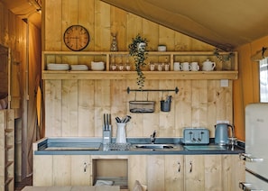 A wooden cabin kitchen with a sink, a kettle, a toaster, and shelves with dishes and a clock. - The Woody Safari Tent (Landford, Nr Salisbury)