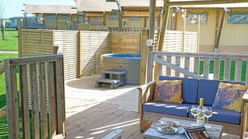 A wooden deck with a hot tub, a sofa with cushions, and a table with plates and glasses.