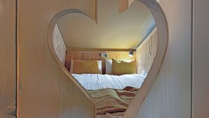 Une chambre avec une découpe en forme de cœur, des murs en bois, un lit avec une literie blanche et une tête de lit dotée d’un luminaire.