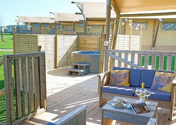 A wooden deck with a hot tub, a sofa with cushions, and a table with plates and glasses.