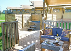 A wooden deck with a hot tub, a sofa with cushions, and a table with plates and glasses.