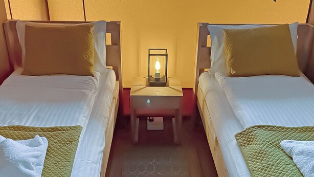 Une chambre d’hôtel avec deux lits, une table de chevet avec une lampe et une fenêtre.