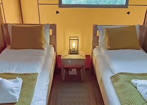 A hotel room with two beds, a nightstand with a lamp, and a window.