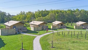 Une rangée de petites cabanes à un seul étage, séparées par un chemin pavé, et entourées d’une zone herbeuse et d’arbres.