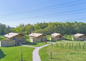A row of small, single-story cabins with a paved walkway between them, surrounded by a grassy area and trees. - The Woody Safari Tent (Pet) (Landford, Nr Salisbury)