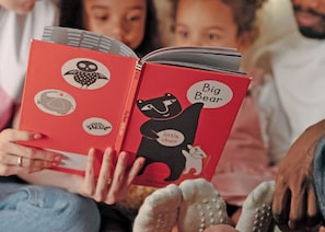 Une personne tenant un livre rouge illustré d’animaux, dont le titre est « Big Bear ».