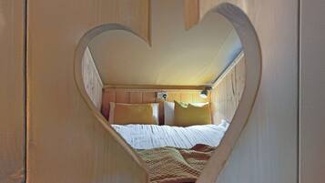 A bedroom with a heart-shaped cutout, wooden walls, a bed with white bedding, and a headboard with a light fixture.