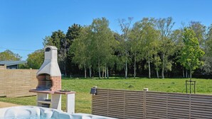 Een hottub, buitenbarbecue en een omheinde tuin met bomen.