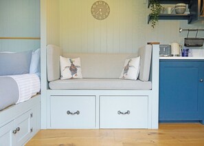 A cozy room with a striped sofa, two pillows, a clock, a kitchen area, and a blue cabinet. - 1 bedroom accommodation in Landford, Nr Salisbury (Landford, Nr Salisbury)