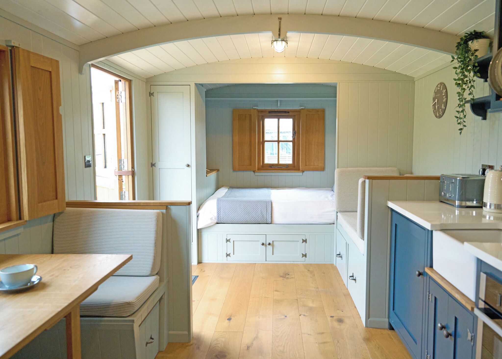 A compact kitchen with a dining area, a small sleeping berth, and a window providing natural light.