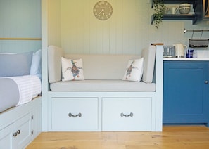 Ein gemütliches Zimmer mit einem gestreiften Sofa, zwei Kissen, einer Uhr, einer Küchenzeile und einem blauen Schrank.
