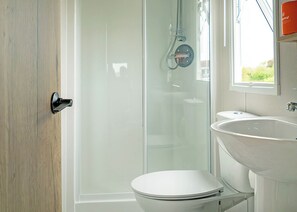 Ein Badezimmer mit Duschkabine aus Glas, einer weißen Toilette und einem Waschbecken mit Spiegel darüber.