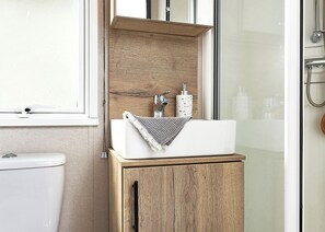 Ein Badezimmer mit weißem Waschbecken, Holzschrank und einer Duschkabine aus Glas.