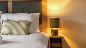 Ein ordentlich bezogenes Bett mit weißen Leinen und gestreiften Kissen, einer Nachttischlampe und einem hölzernen Kopfteil.