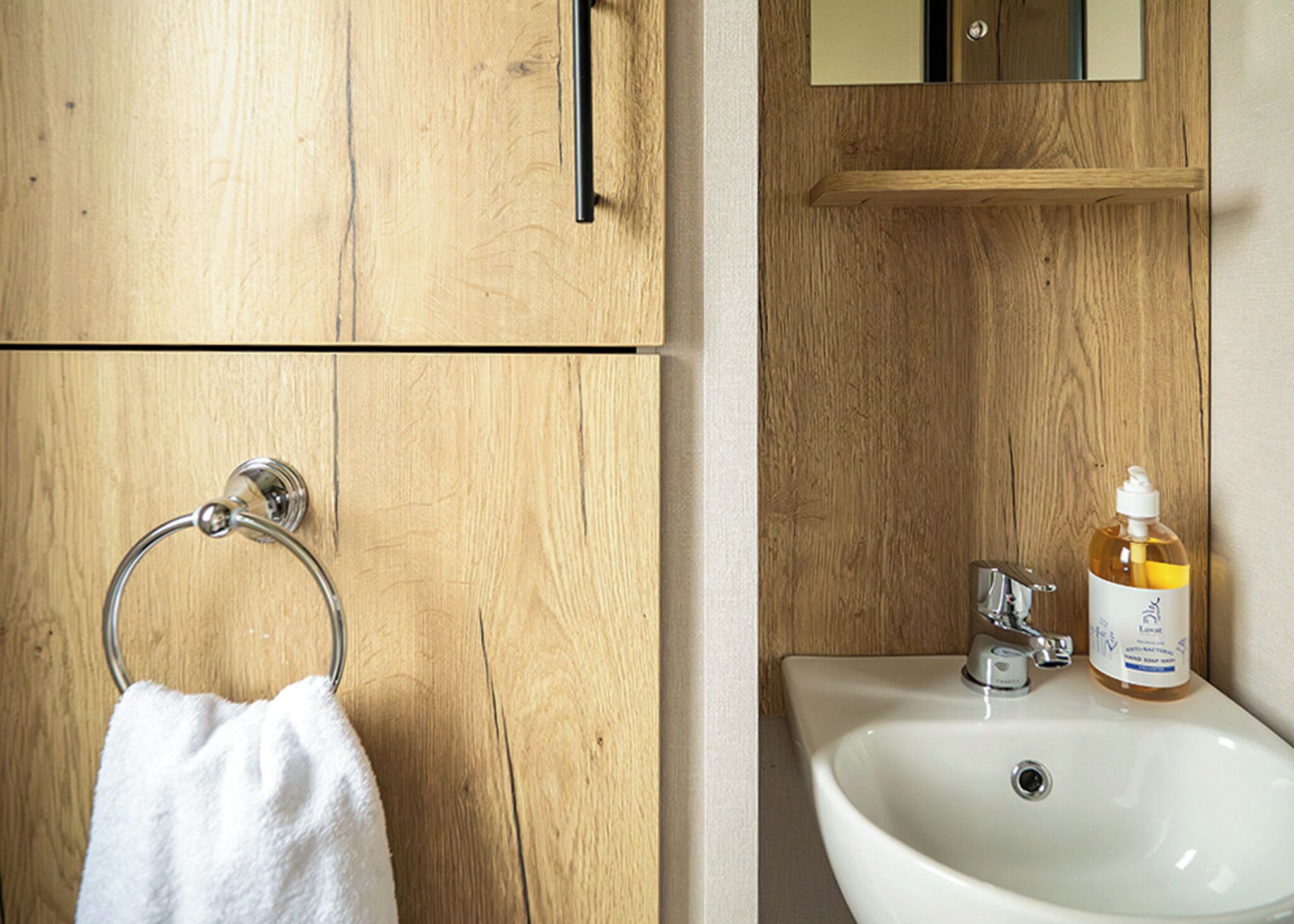Une salle de bain en bois avec un lavabo blanc, un porte-serviette et un flacon de savon.