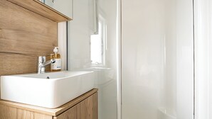 Un bagno con un lavandino bianco, mobili in legno e box doccia in vetro.