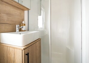 A bathroom with a white sink, wooden cabinets, and a glass shower enclosure. - The Superior 3 Bed is a comfortable and spacious sleeps 8 caravan. (Great Yarmouth)