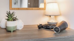 Un comodino in legno con una lampada, un asciugacapelli e una pianta in vaso.