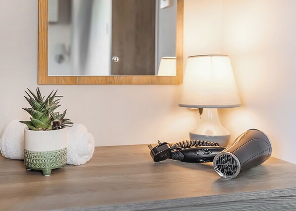 Une table de chevet en bois, avec une lampe, un sèche-cheveux et une plante en pot.