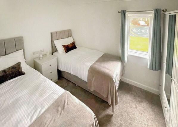 A bedroom with two beds, a nightstand, a window with curtains, and a radiator.