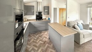 Une cuisine moderne avec des meubles gris, un four encastré et un sol à motifs en chevrons.