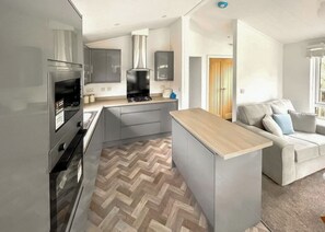 Une cuisine moderne avec des meubles gris, un four encastré et un sol à motifs en chevrons.