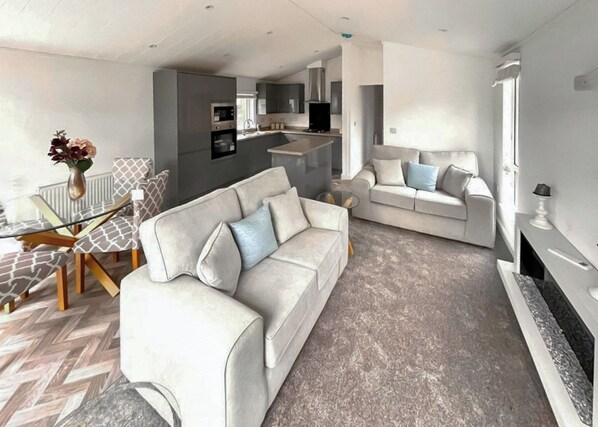 A modern living room with a sofa, a coffee table, and a fireplace. - New to hire for the 2025 season is this beautiful Lakeland lodge. (Eamont Bridge)