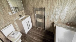 Une salle de bain avec un plancher en bois, un lavabo blanc, un miroir et un porte-serviettes.
