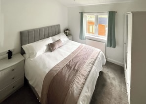 A bedroom with a bed, a nightstand, a dresser, a window with curtains, and a radiator. - New to hire for the 2025 season is this beautiful Lakeland lodge. (Eamont Bridge)