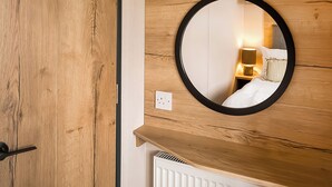 Eine Holzwand mit einem runden Spiegel, der ein Bett und einen Nachttisch mit einer Lampe widerspiegelt.