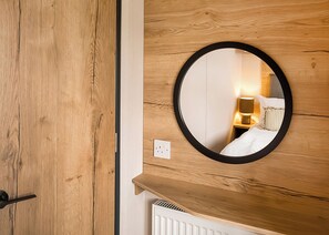 A wooden wall with a round mirror reflecting a bed and a nightstand with a lamp. - Superior 3 Bed (Pet) (Great Yarmouth)