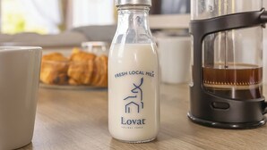 Eine Flasche frische, regionale Milch, eine Kaffeemaschine und Gebäck auf einem Holztisch.