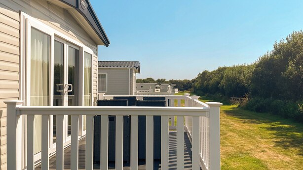 Een stacaravan met terras, een overdekt buitenverblijf en uitzicht op de omliggende groen.'