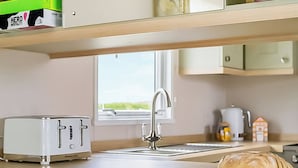 Een kitchenette met een broodrooster, een spoelbak, een raam en een brood op het aanrecht.