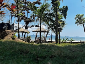 Una playa con chozas de techo de paja, palmeras y vista al mar.
