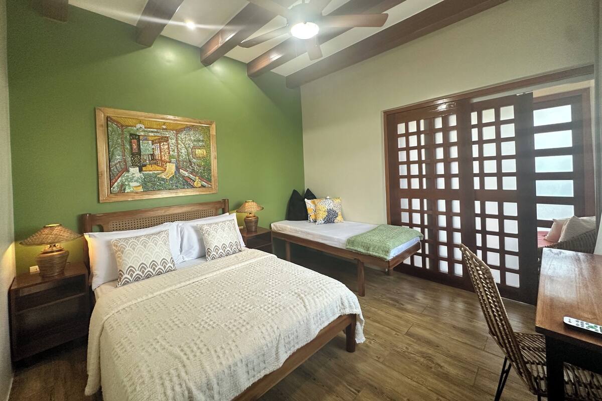 Un dormitorio con una cama, dos mesitas de noche, una lámpara, una silla, un separador de madera y un ventilador de techo.