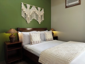 Een net opgemaakt bed met gekleurde kussens, een bedlampje en een wanddecoratie van macramé.