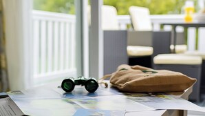 Ein Tisch mit Feldsteuerre, einer braunen Tasche und einer Zeitung, im Hintergrund ist ein Balkon mit Stühlen zu sehen.