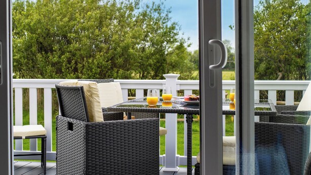 Eine Terrasse mit Korbmöbeln, einem Glastisch und einem weißen Geländer.