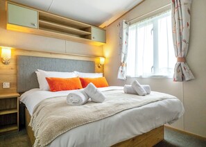 Une chambre d’hôtel comprenant un lit, des oreillers, une table de chevet, une lampe, une fenêtre avec des rideaux et des étagères intégrées.